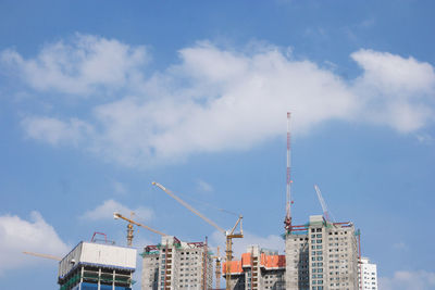 Low angle view of crane and buildings against sky