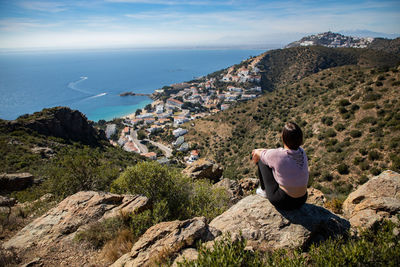 Rear view of woman sitting on rock against sea and sky