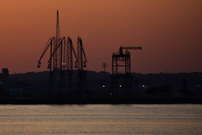 Silhouette cranes at pier against sky during sunset