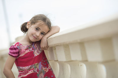 Portrait of smiling girl leaning retaining wall