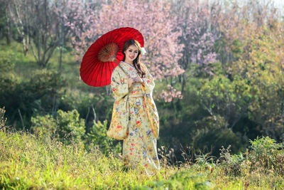 Woman with red umbrella standing by plants