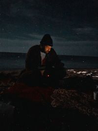 Couple sitting on sea shore against sky at night