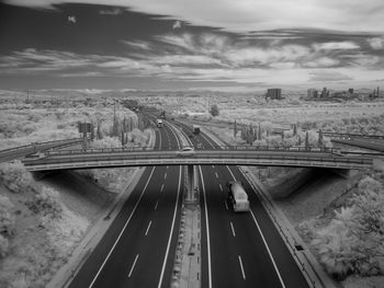 Infrared image of bridge over road against cloudy sky