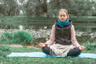 Portrait of woman sitting by lake against trees