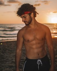 Midsection of shirtless man standing at beach against sky