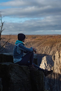 Rear view of man sitting on rock against sky