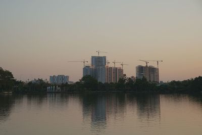 Buildings by river against sky during sunset