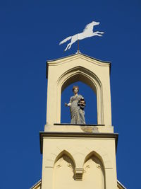 Low angle view of statue against blue sky and building