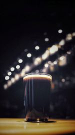 Close-up of dark beer in glass on table with blurred bar lights in the background