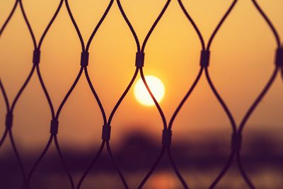 Silhouette chainlink fence against sky during sunset