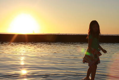 Woman standing on beach against sky during sunset