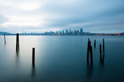 Wooden posts in lake against cloudy sky