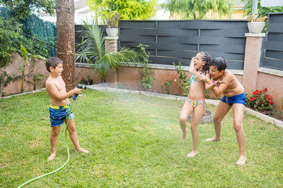 Three funny kids playing with a hose in the garden