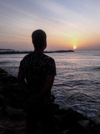 Rear view of man looking at sea against sunset sky