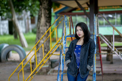 Portrait of young woman standing against outdoor play equipment