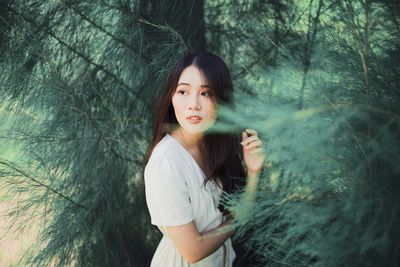 Beautiful young woman looking away by trees in forest