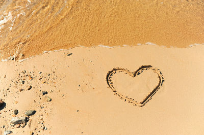 Painted heart on clean sand of beach and a wave of clear transparent water rolls, not glossy image