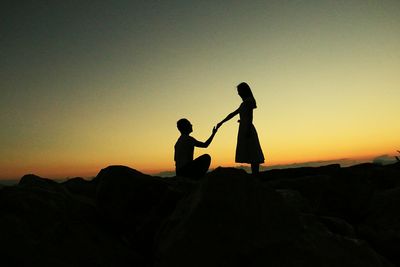 Silhouette couple on field against sky during sunset