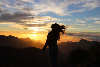 Silhouette young woman standing on mountain against sky during sunset