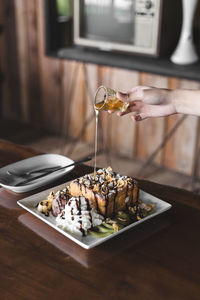 Cropped hand of woman pouring sauce on ice cream in plate