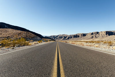 Road leading towards mountains against clear sky