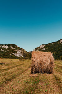 Hay bales on field against clear blue sky