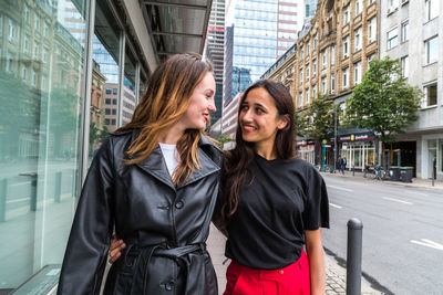 Young women standing with arm around on footpath in city 