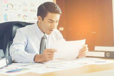 Happy businessman reading document at desk in office