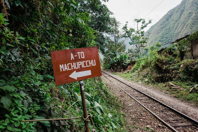 Information sign by railroad tracks by trees