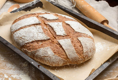 Baked oval rye flour bread in a metal baking sheet on the table, top view