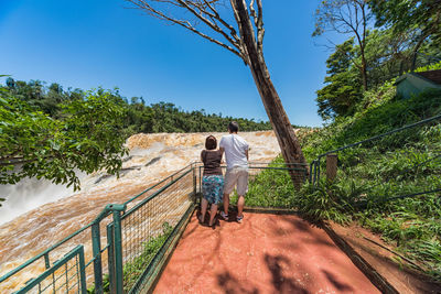 Rear view of couple standing by railing against waterfall