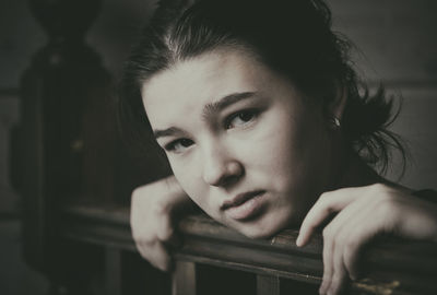Portrait of depressed girl leaning on wooden railing at home