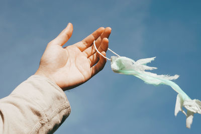 Close-up of hand holding ripped surgical mask against sky