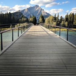 Wooden footbridge leading towards mountains against sky