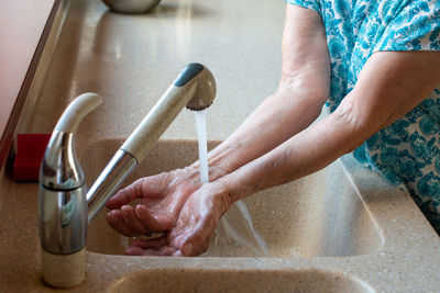 Senior woman's hands under cold running water. close up. how to stay cool in hot weather. 