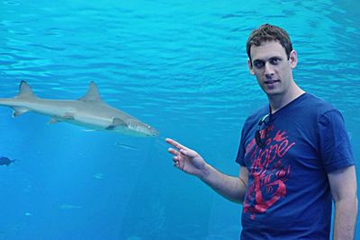 Portrait of man gesturing at shark fish swimming in tank at aquarium