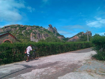Man riding bicycle on road by mountain against sky