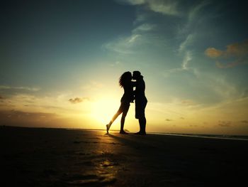 Silhouette woman standing on beach against sky during sunset