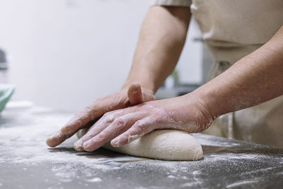 Male chef kneading flour dough on kitchen counter in bakery