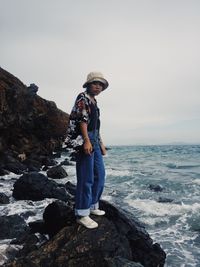 Full length of man standing on rock at sea shore against sky