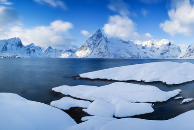 Frozen lake and snowcapped mountains against sky