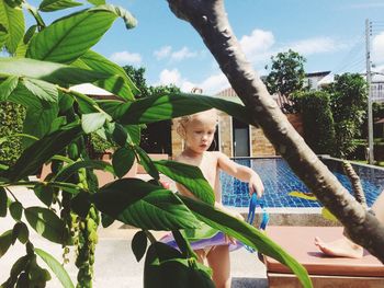 Girl standing by plant at poolside on sunny day