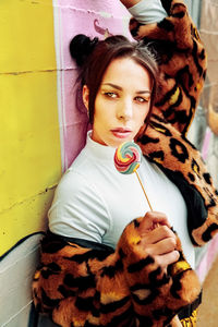 Portrait of young woman holding lollipop while standing against wall