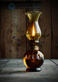 Close-up of lit candle on table against illuminated wall