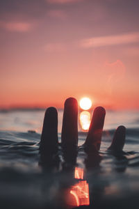 Close-up of hands against sea during sunset