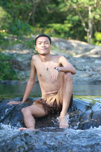 Portrait of young man sitting on rock in stream