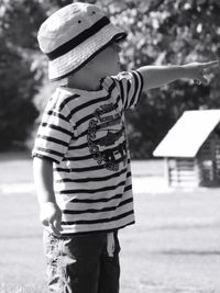 Rear view of boy holding hat standing against tree