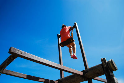Low angle view of mid adult woman swinging against clear blue sky