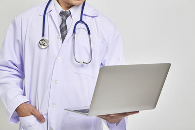 Midsection doctor holding laptop against white background