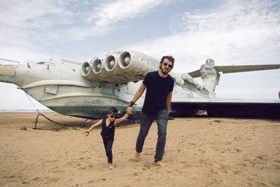 Family boy and his father in rocker clothes stand an abandoned ekranoplan plane by sea in dagestan